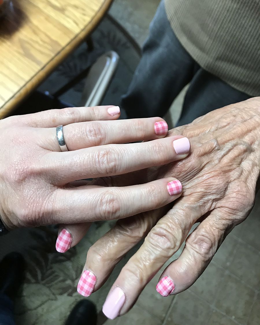 Erika’s hand resting on an older woman’s hand; both have pink painted nails.