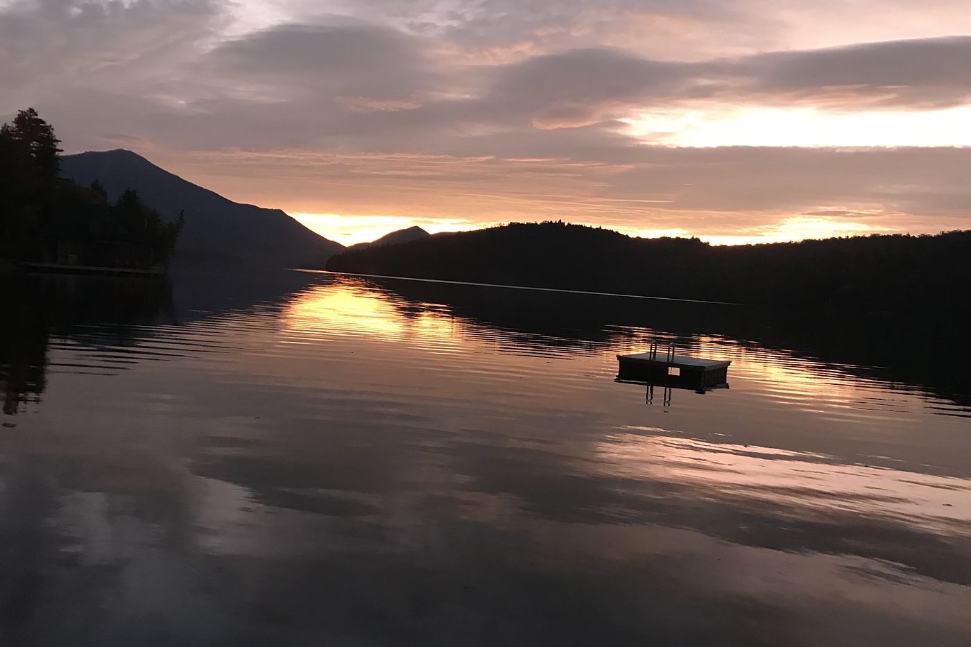 A still lake at dusk, the last light glowing behind a dark mountain.