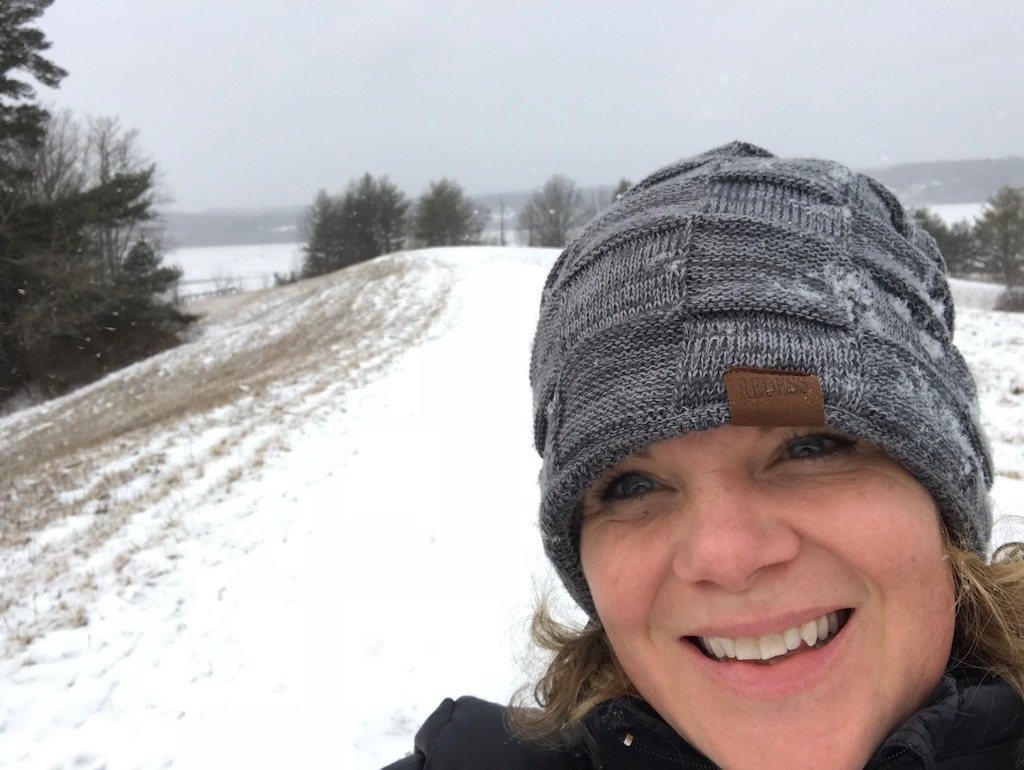 Erika smiling in a knit winter hat on a snowy hillside path.
