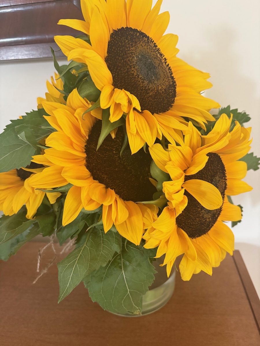 A bunch of bright sunflowers in a glass vase on a wooden table.